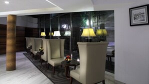 A lobby with four armchairs, a small table with a vase, and lamps. - Hiltop Hotel (Mumbai)