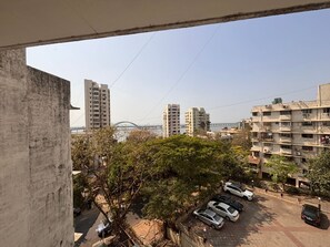 A residential area with multi-story buildings, a parking lot with several cars, and a bridge in the background. - Hiltop Hotel (Mumbai)
