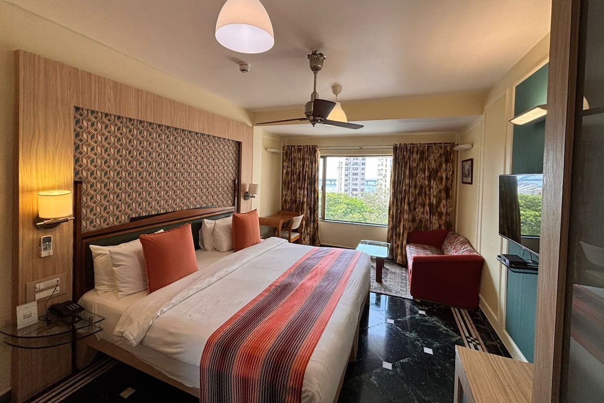 A hotel room with a bed, a desk, a chair, a TV, and a window with curtains.