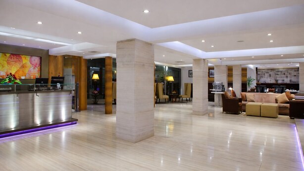 A spacious lobby with a reception desk, seating area, and a large pillar. - Hiltop Hotel (Mumbai)