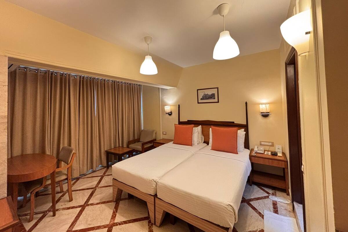 A hotel room with a double bed, a desk with a chair, a small table, a telephone, and a picture on the wall.
