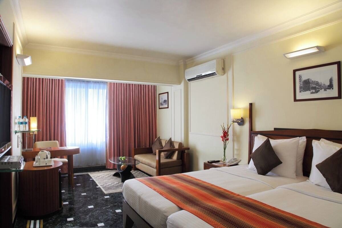 A hotel room with a bed, a desk, a chair, a TV, and a window with curtains.