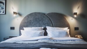 A neatly made bed with white linens and a grey headboard, accompanied by two wall-mounted light fixtures. - The Circus Hotel (Berlin)