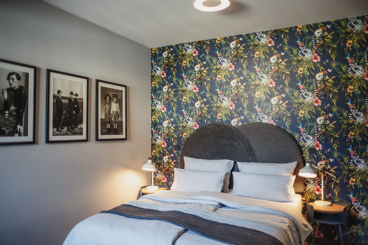 Ein Schlafzimmer mit einem Bett, Nachttischen, gerahmten Bildern an der Wand und floralem Wandpapier.