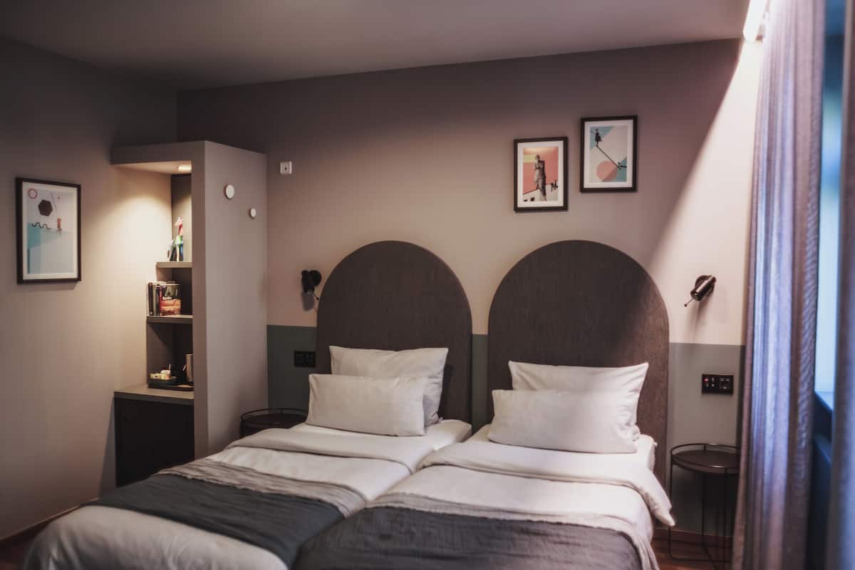 Ein Doppelbett mit zwei Kissen, ein Nachttisch, ein kleiner Stuhl. An der Wand befinden sich zwei gerahmte Bilder.