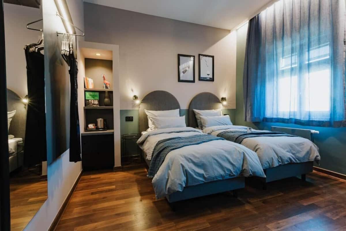 Ein Schlafzimmer mit zwei Betten, einem Nachttisch, einem Regal mit Gegenständen und einem Fenster mit Vorhängen.