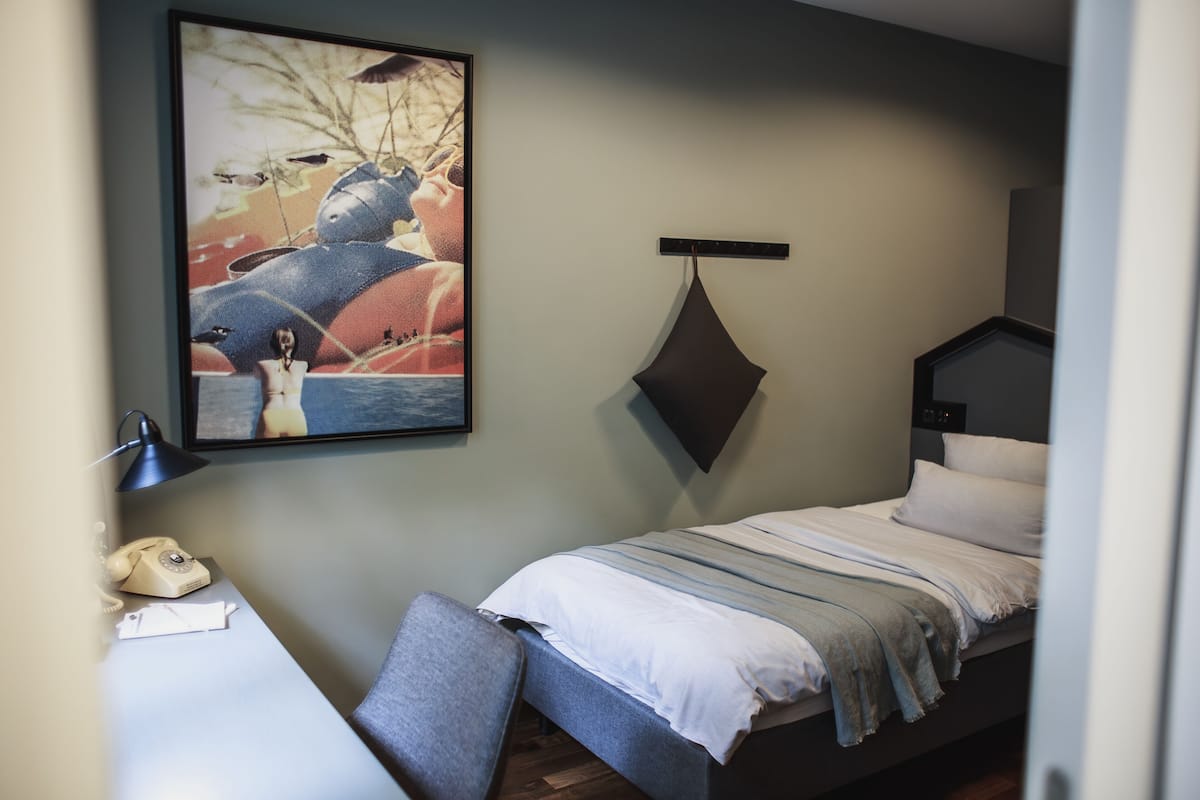 Ein Schlafzimmer mit einem Bett, einem Schreibtisch, einem Stuhl, einer Pendelleuchte und einem Bild an der Wand.