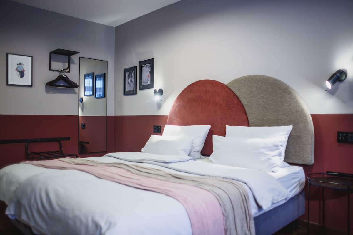 Ein Hotelzimmer mit Bett, Spiegel, Kleiderhaken und Wandleuchten.