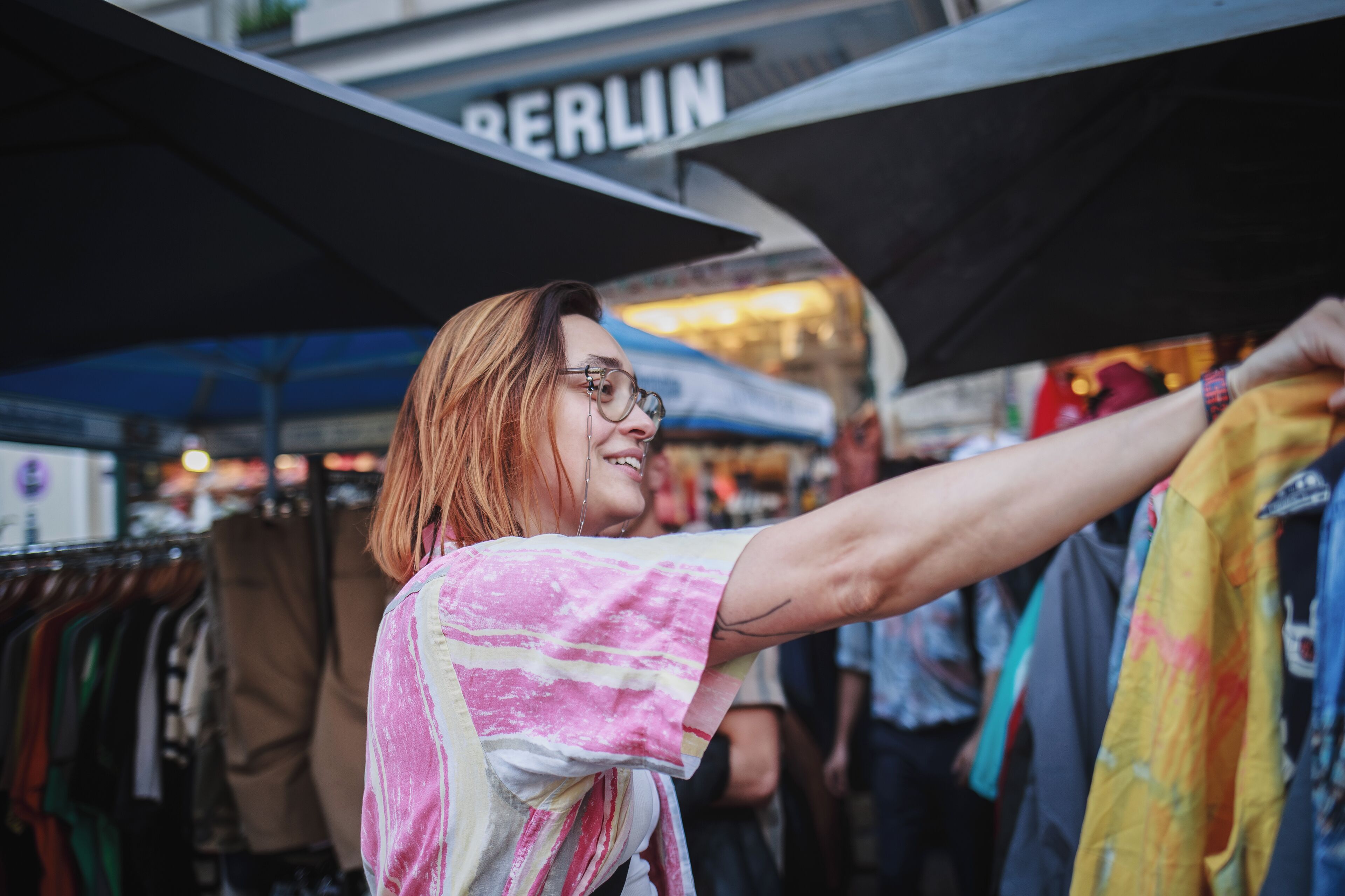 Una persona hojea ropa en un mercado al aire libre, con un cartel que dice "BERLIN" al fondo.