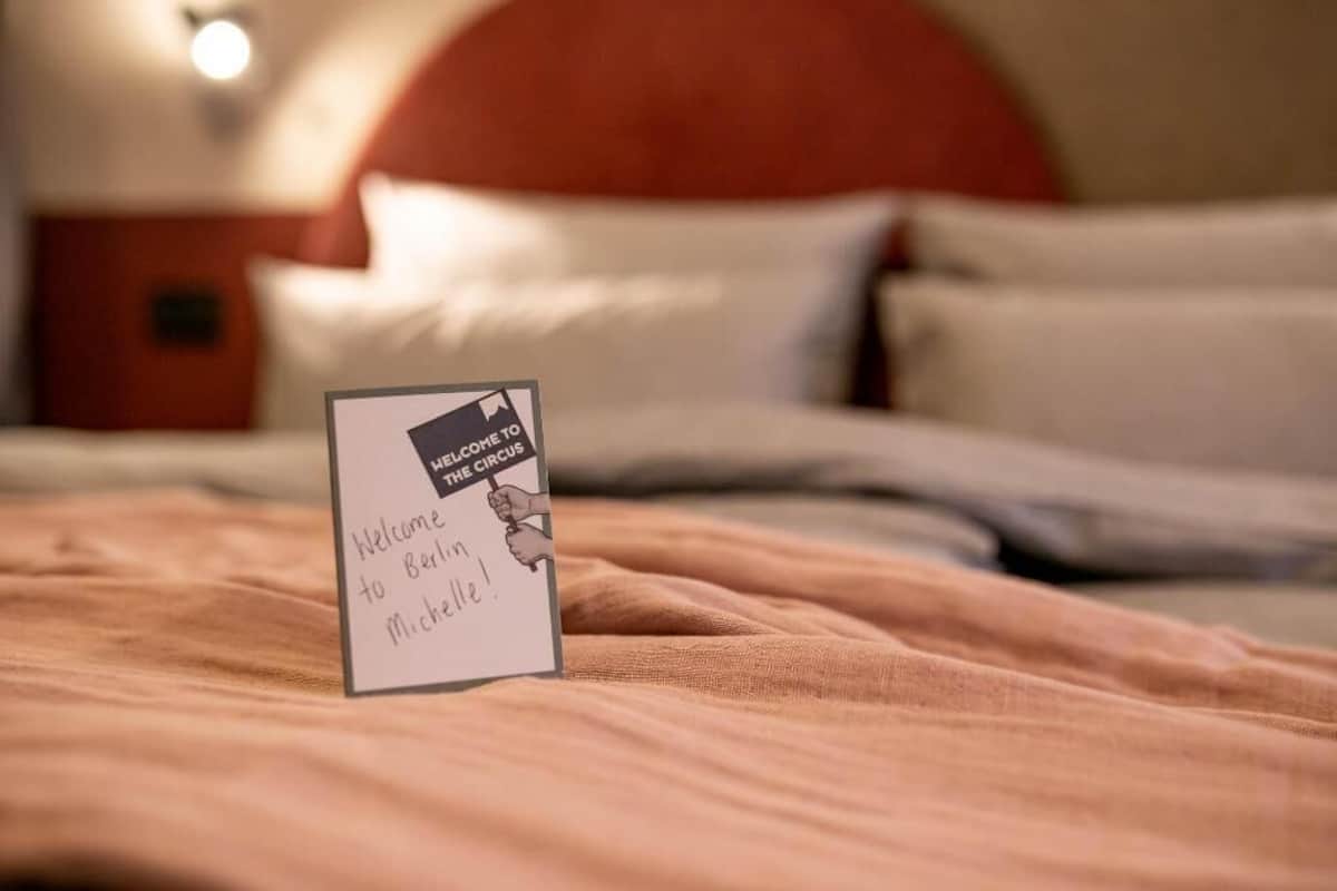 Ein Bett mit einem Schild, auf dem 'Willkommen in Berlin, Michael!' steht, in einem Hotelzimmer.