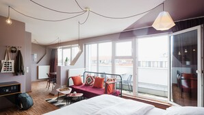 Ein modernes Hotelzimmer mit einem großen Bett, einem Schreibtisch, einem Sessel und einem Balkon mit Blick.