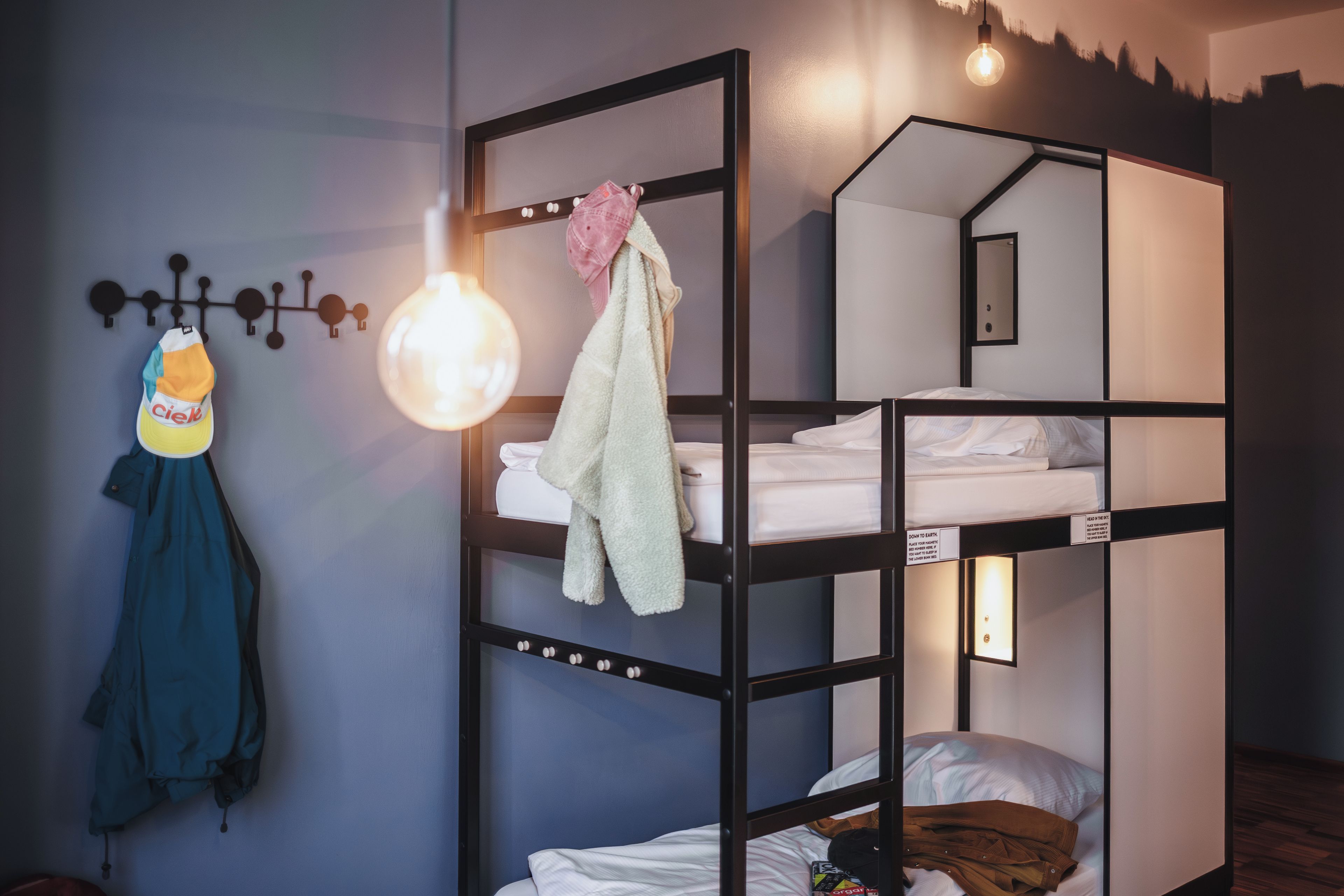 Habitación con literas, una lámpara colgante, una toalla y una chaqueta en la pared.