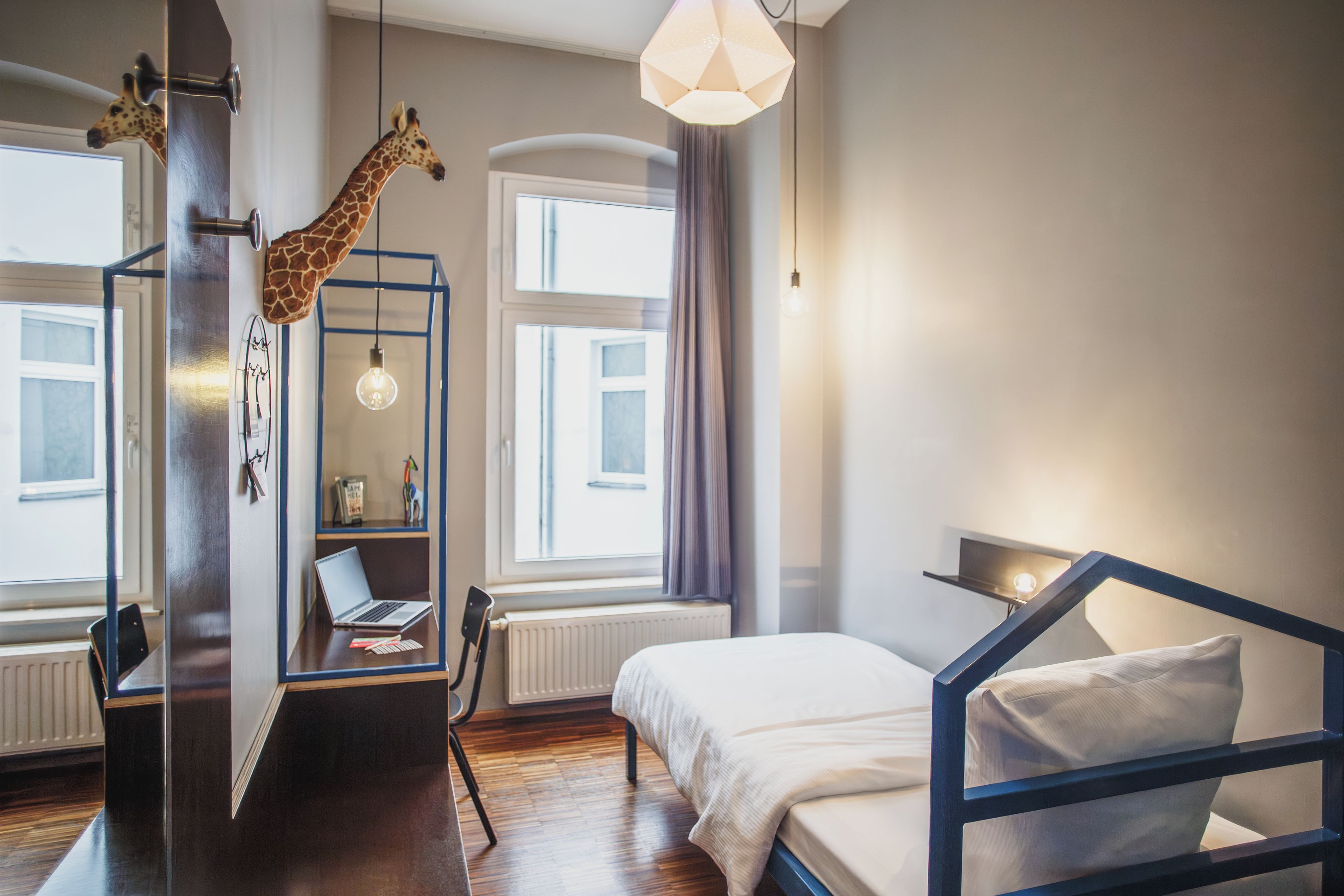 Ein Schlafzimmer mit einem Bett, einem Schreibtisch, einem Stuhl, einem Laptop und einer Giraffen-Dekoration.