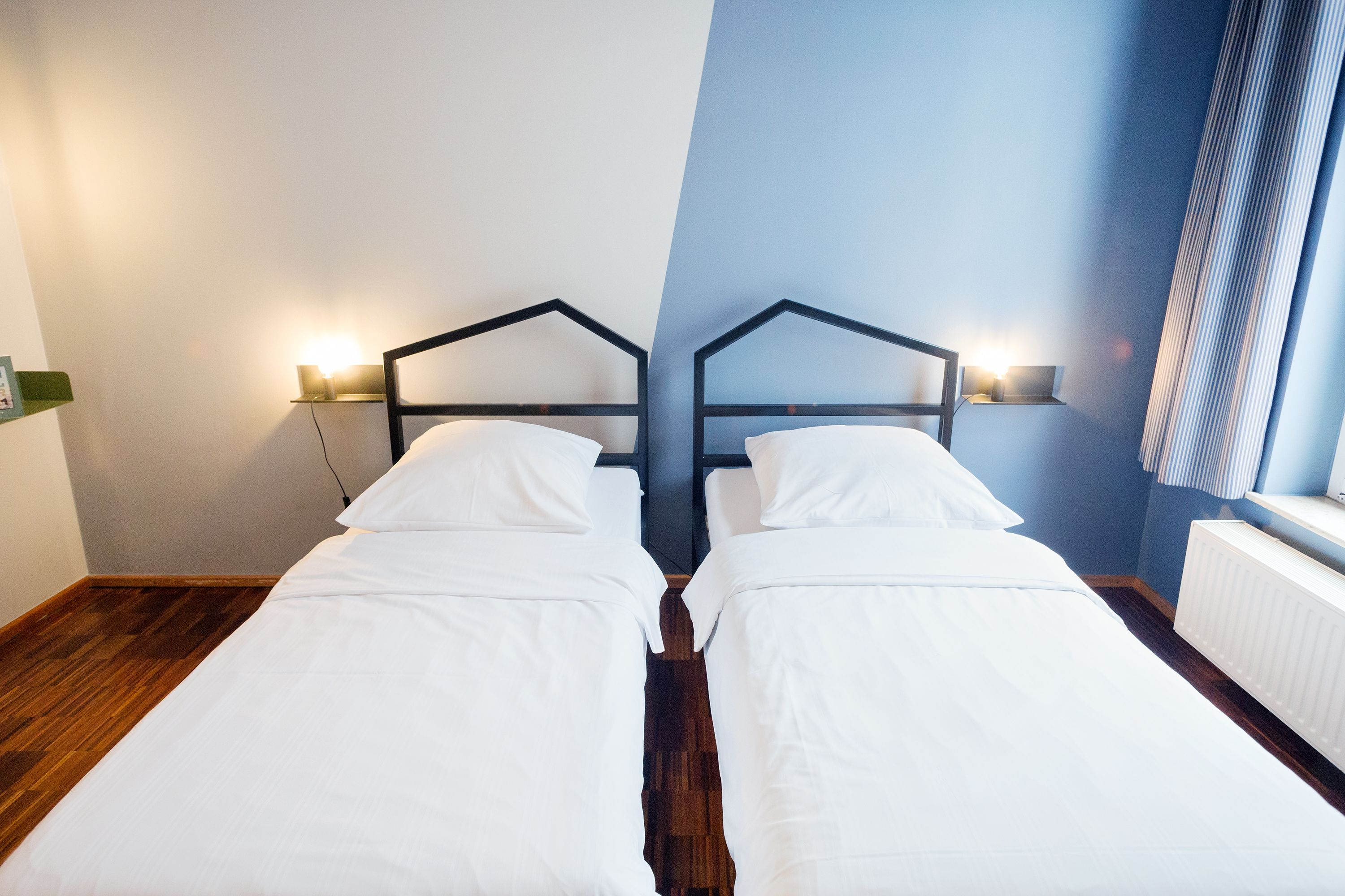 Habitación de hotel con dos camas individuales, suelo de madera, un radiador blanco y una pared azul.