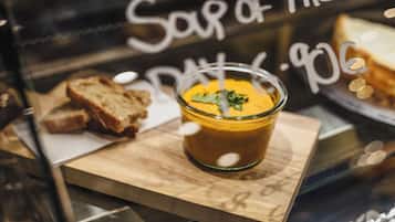 A glass of soup with a garnish on a wooden board, with bread and a sign in the background.