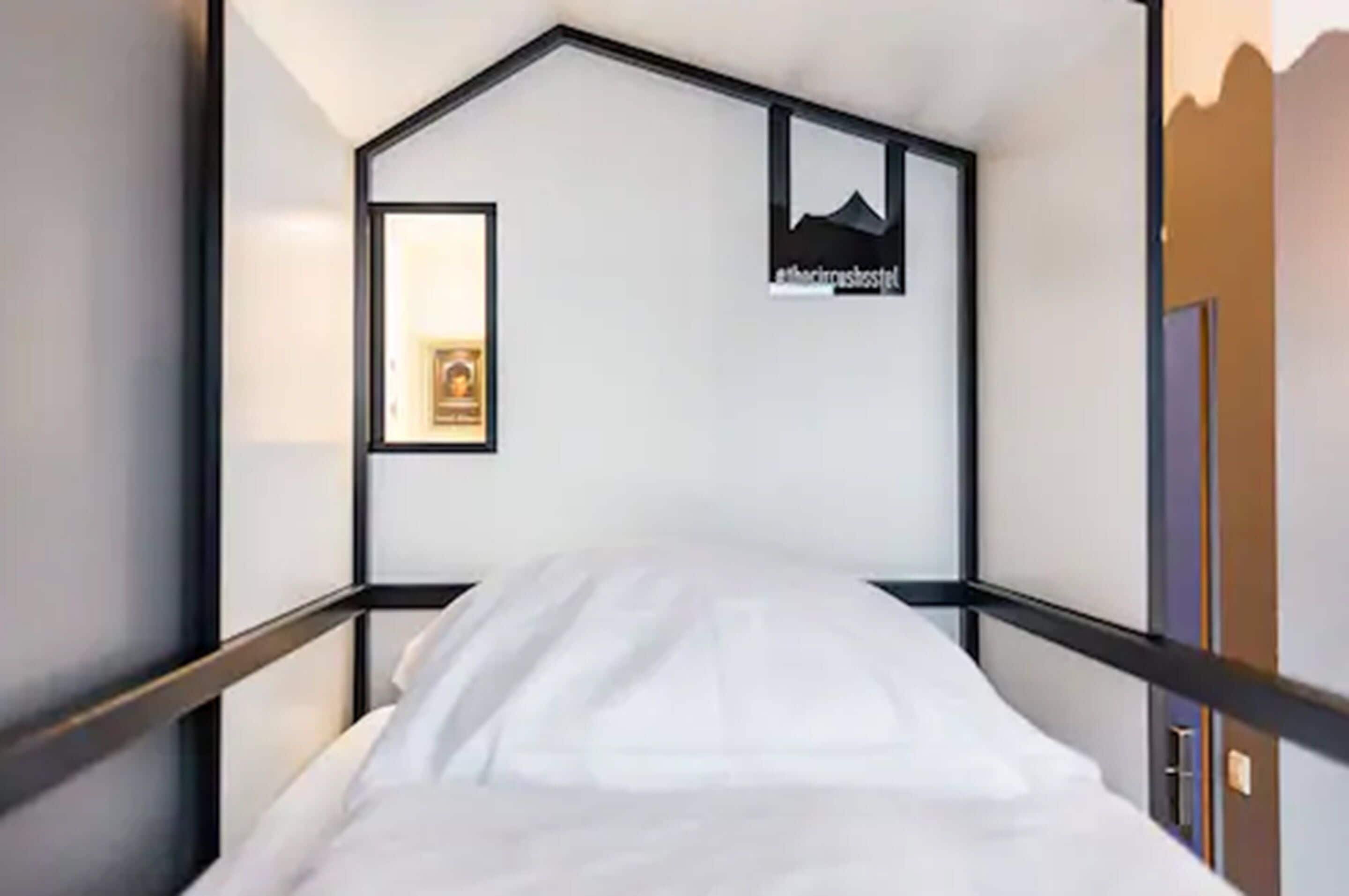 A single bed in a room with a simple, modern design. There is a framed picture on the wall and a sign with text.