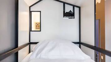 A single bed in a room with a simple, modern design. There is a framed picture on the wall and a sign with text.