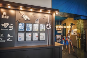 Eine Rezeption mit gerahmten Informationsplakaten, einer Giraffendeko und einem Schild mit der Aufschrift 'The Circus Hostel'.