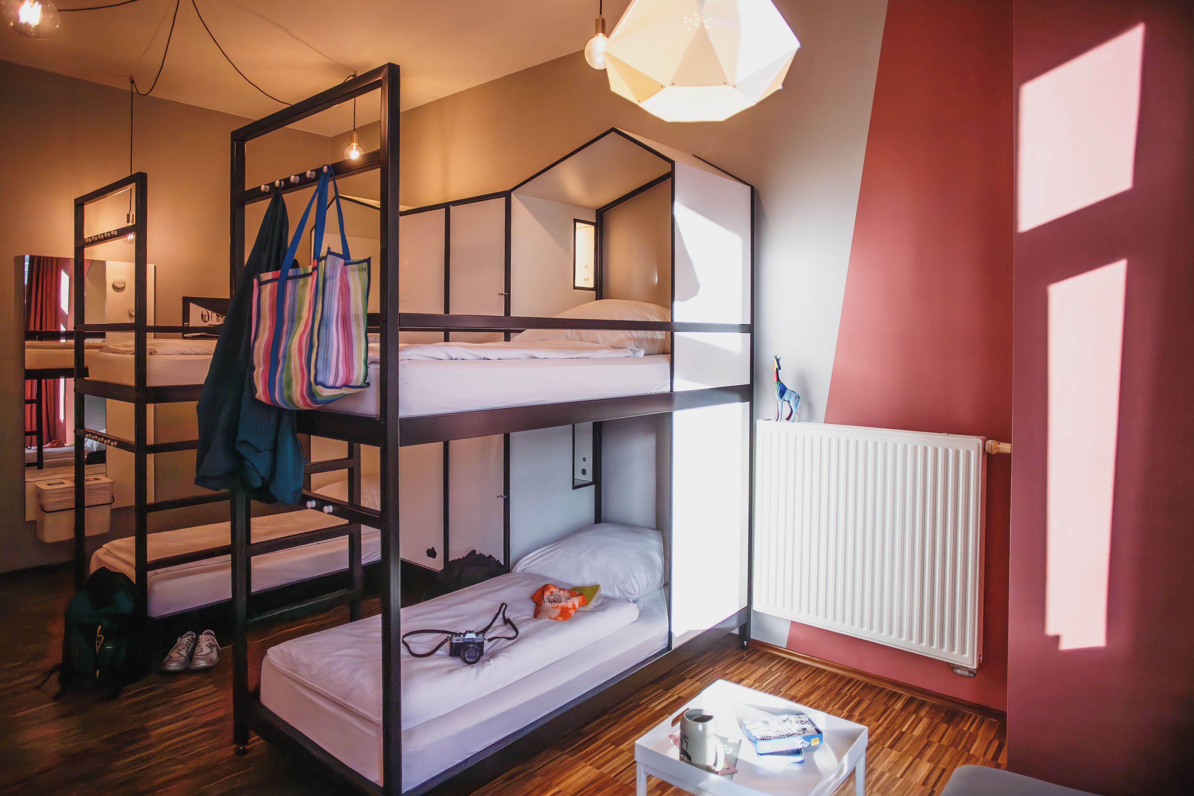 Een slaapkamer met een stapelbed, een houten trap, een witte radiator en een klein tafeltje met een kop en een boek.