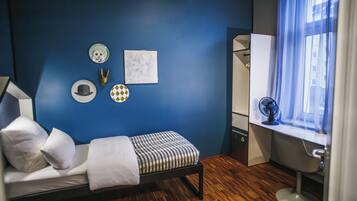 Un dormitorio con cama, escritorio, silla, ventana con cortinas, y pared decorada con platos y un cuadro.