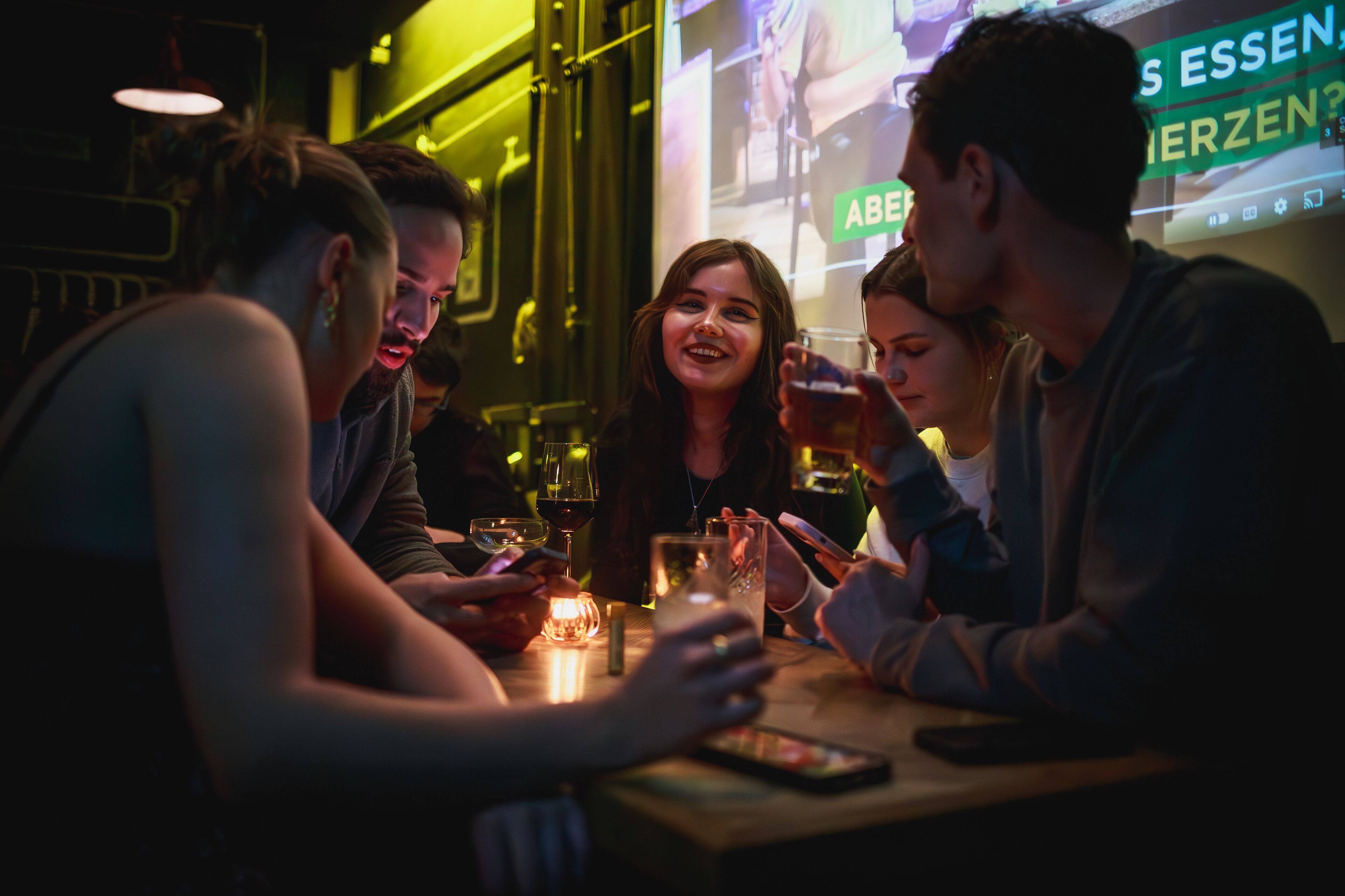 Un grupo de personas sentadas alrededor de una mesa en un espacio interior con poca luz, posiblemente un bar o restaurante.