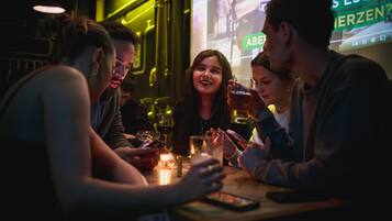 Un grupo de personas sentadas alrededor de una mesa en un espacio interior con poca luz, posiblemente un bar o restaurante.
