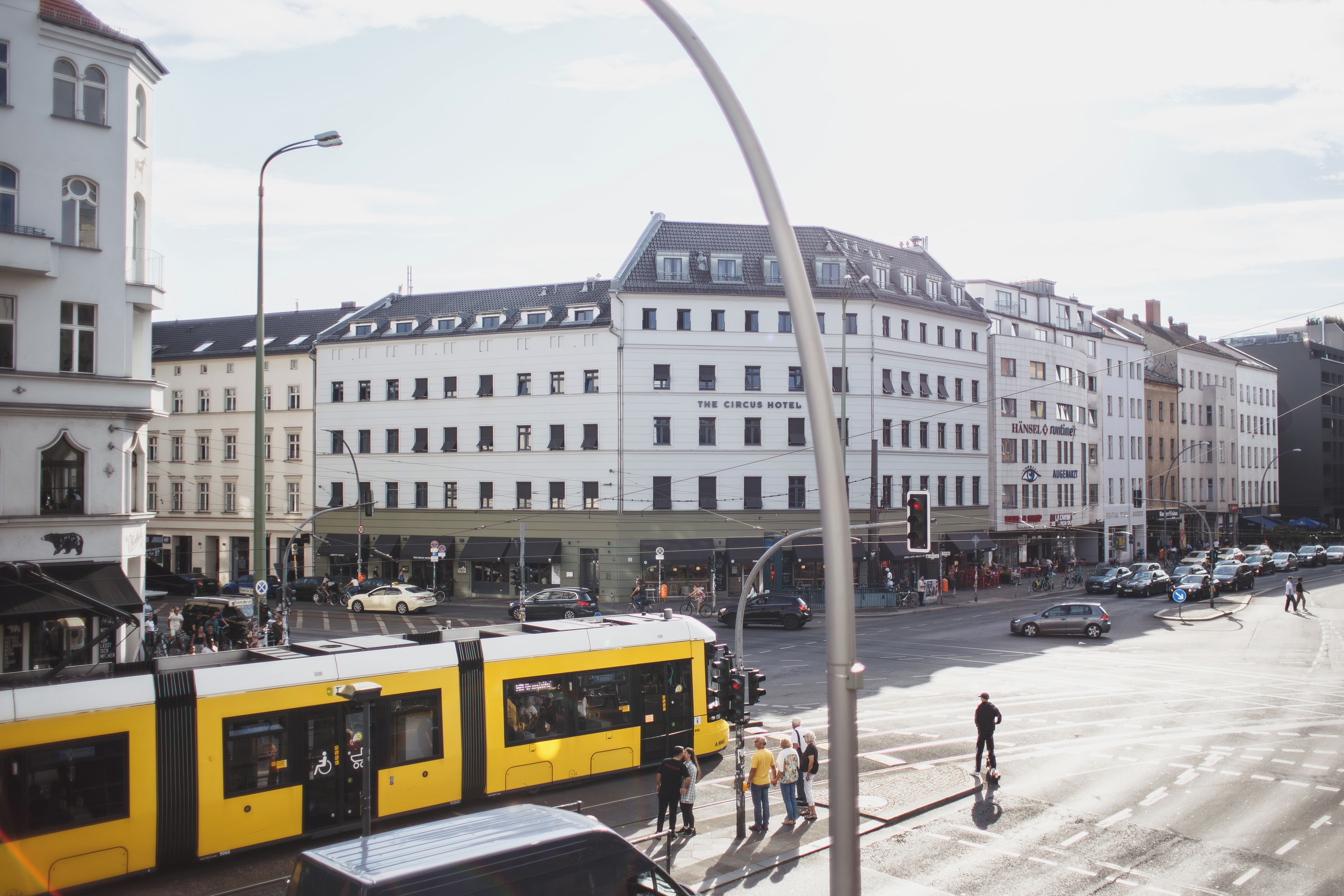 Une vue de rue avec un bâtiment portant l’inscription « The Circus Hotel » et un tramway jaune.
