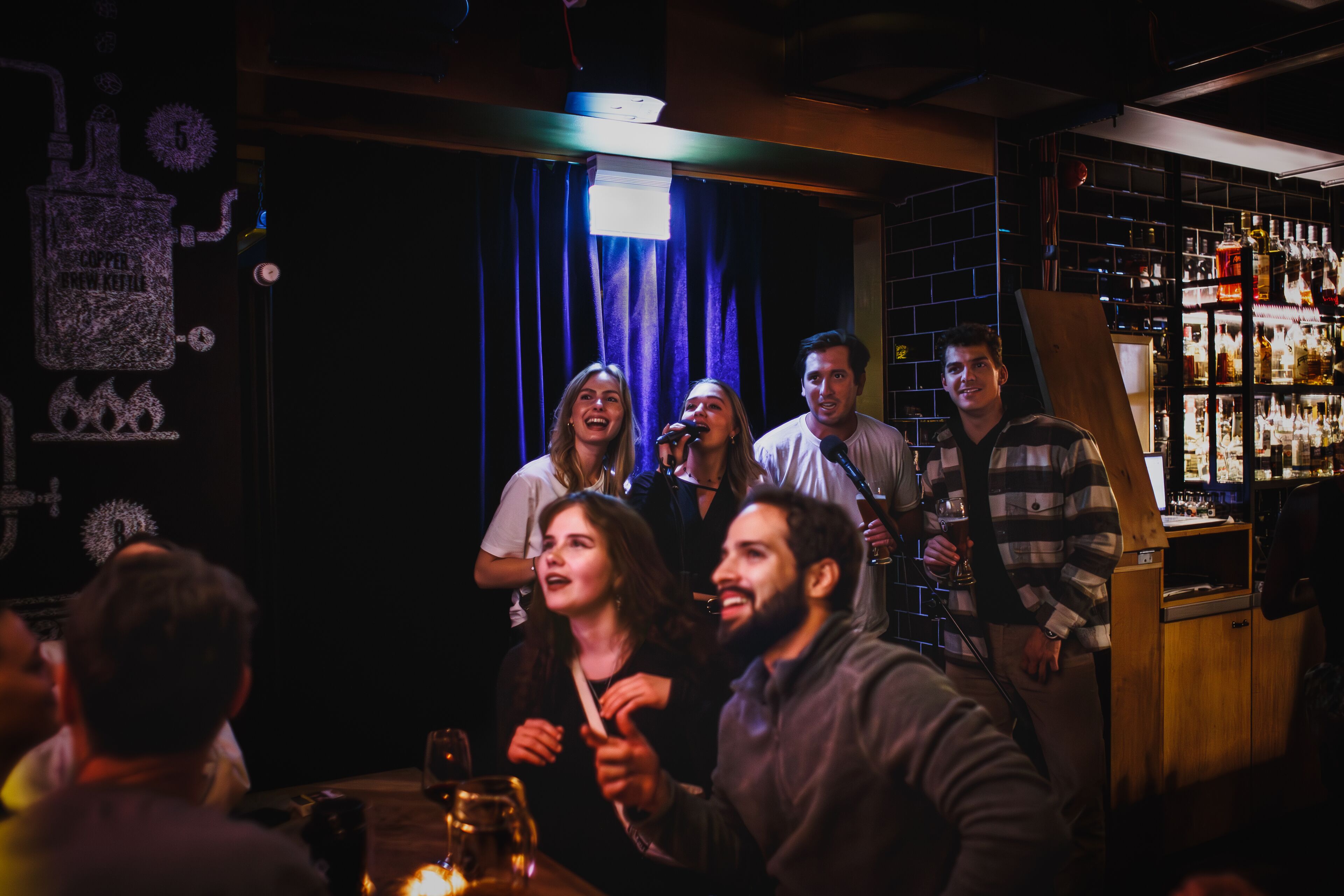 Un bar con interior oscuro, una barra de madera y una estantería con botellas.
