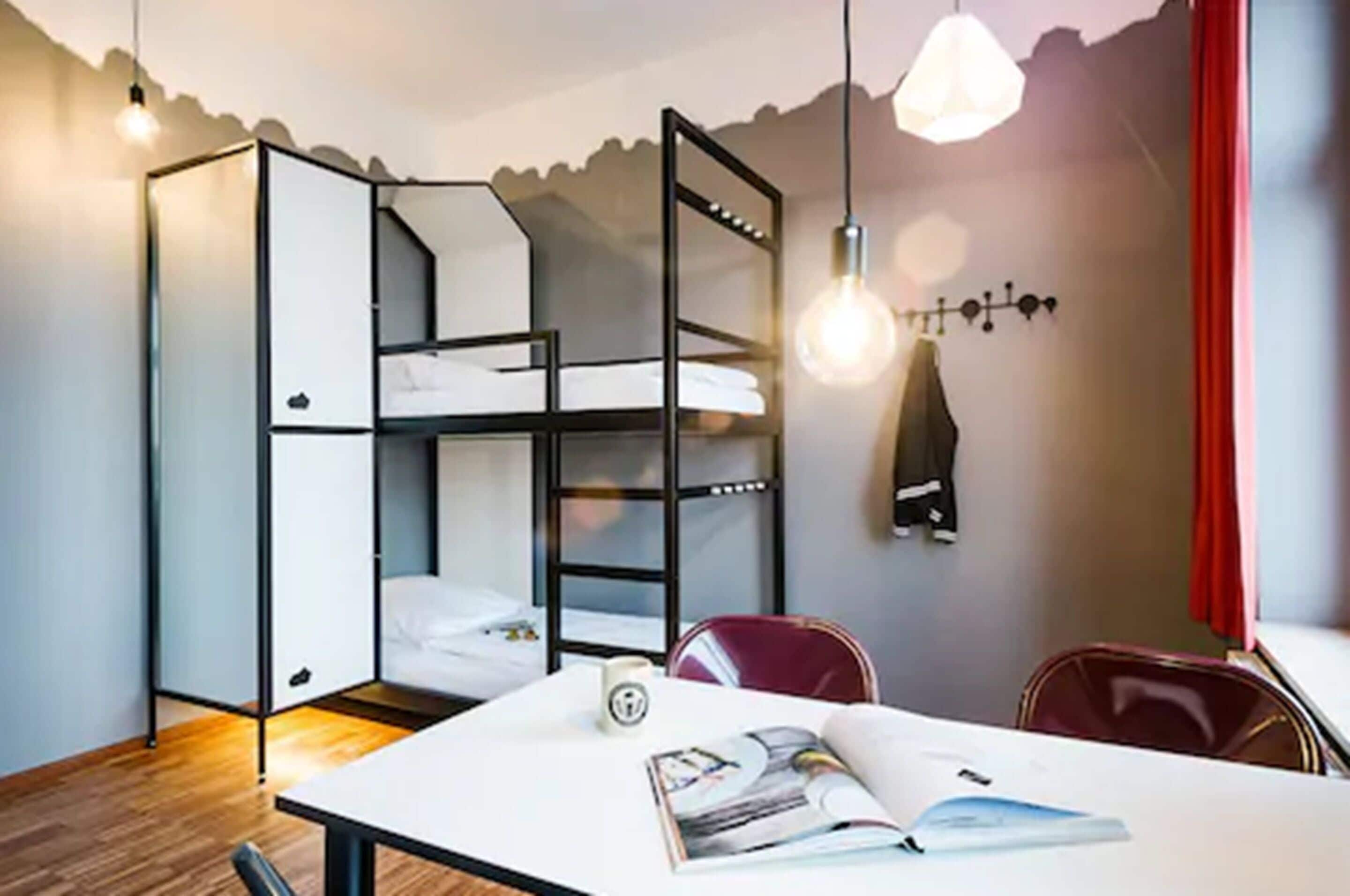 Una habitación pequeña con una cama nido, una mesa con una revista y una silla roja.