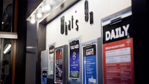 Eine Wand mit beleuchteten Buchstaben, die 'What's On' zeigen, und mehrere Werbeplakate, die Veranstaltungen und Dienstleistungen bewerben.