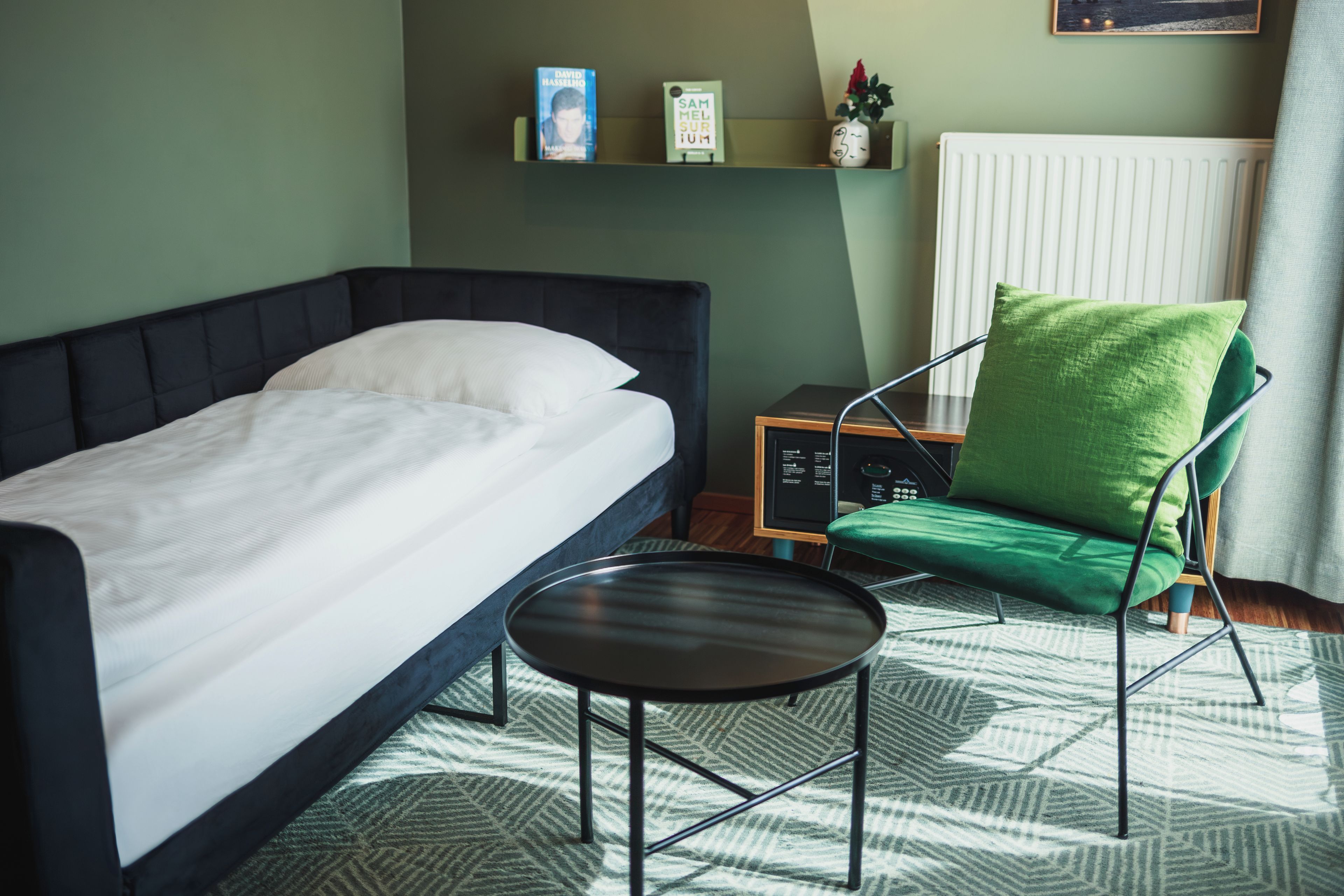 Un dormitorio con una cama, una silla, una mesita y un radiador.