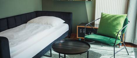 Un dormitorio con una cama, una silla, una mesita y un radiador.