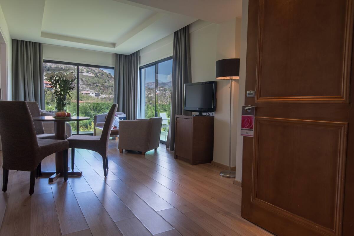 Ein Hotelzimmer mit Essbereich, Fernseher und großem Fenster mit Blick ins Freie.