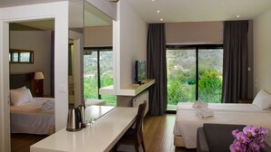 A hotel room with two beds, a desk, a TV, and a large window with a view of greenery. - Rodon Hotel and Resort (Agros)