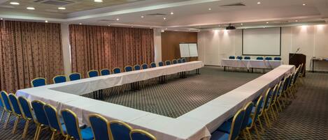 Une salle de conférence avec une longue table, des chaises bleues, un tableau blanc et un écran de projection.