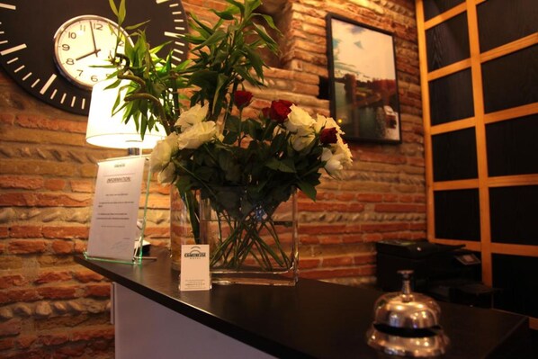 A reception desk with a clock, a vase of flowers, and a framed picture on the wall.