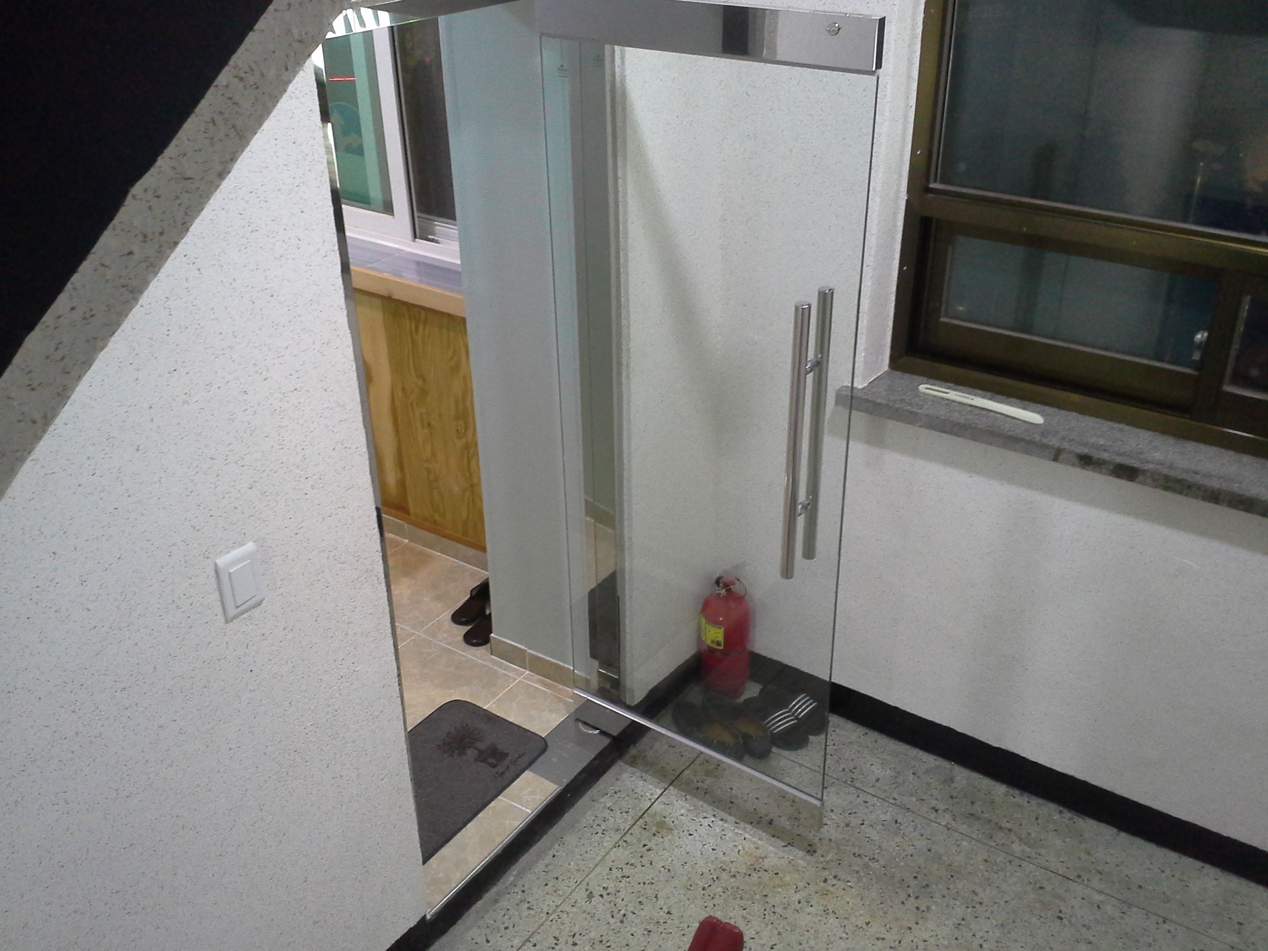 A kitchen with a glass door, a fire extinguisher, and a mat at the entrance.