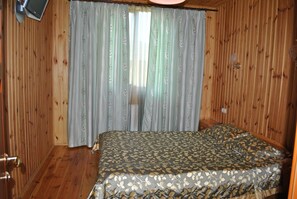 A room with wooden panel walls, a bed with a patterned bedspread, and a curtain with a leaf pattern. - Elki-Palki (Sovinion)