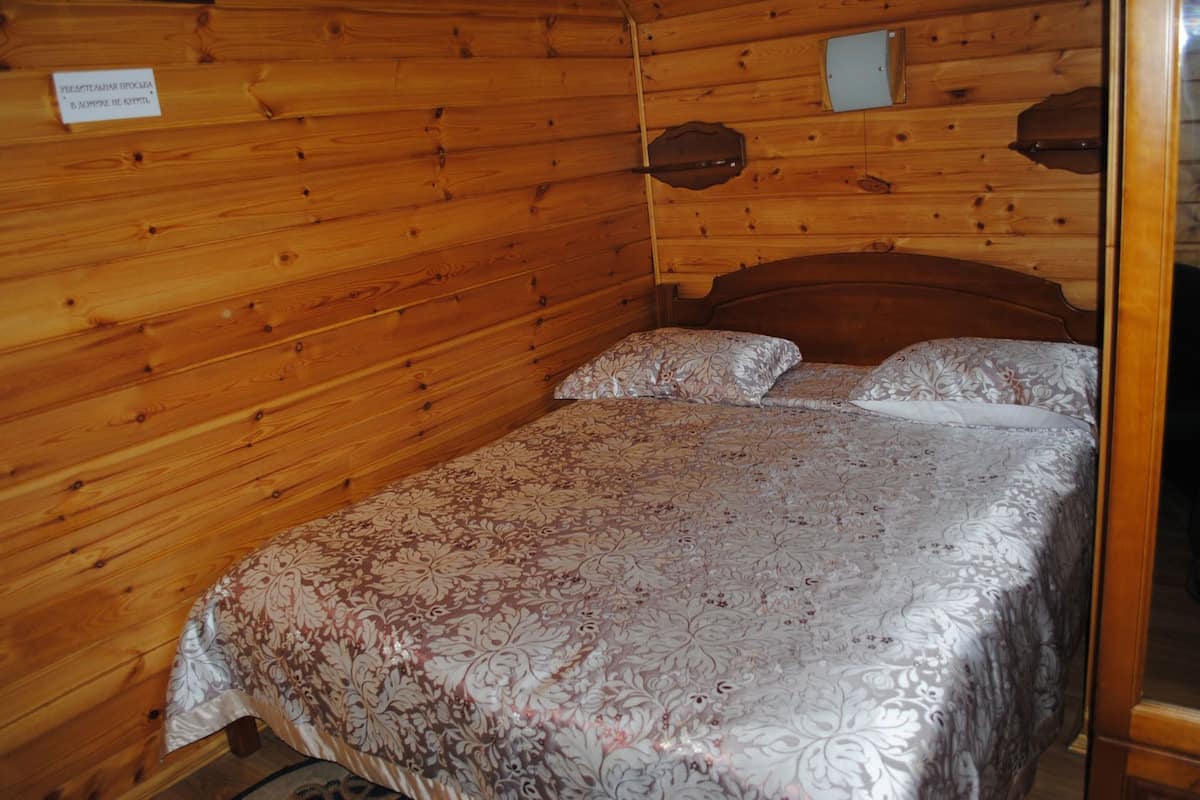 A wooden-paneled room with a bed, a small table, and a wall-mounted shelf.