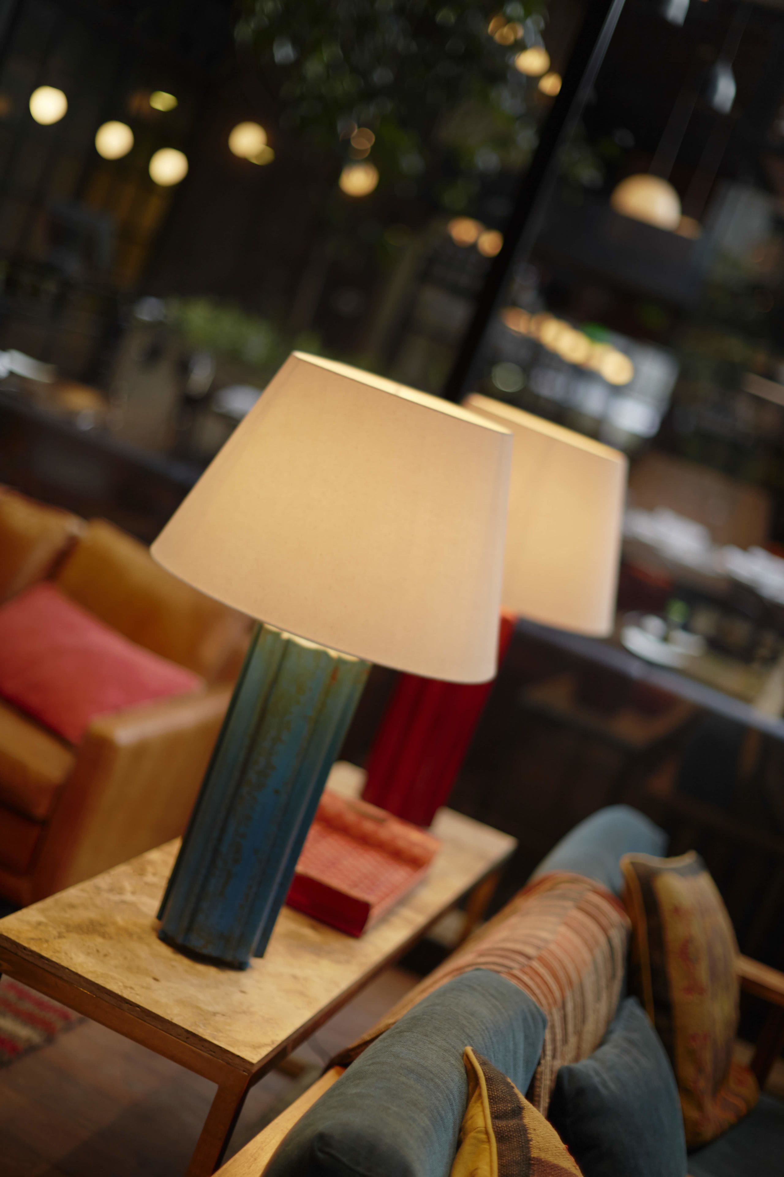 Un área de estar bien iluminada, con dos lámparas sobre una mesa de madera, un sofá con cojines y vistas al interior.