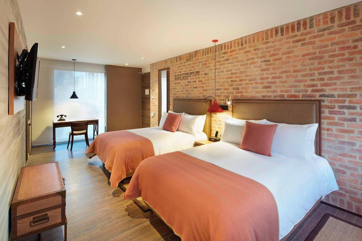 A hotel room with two beds, a desk, and a TV.