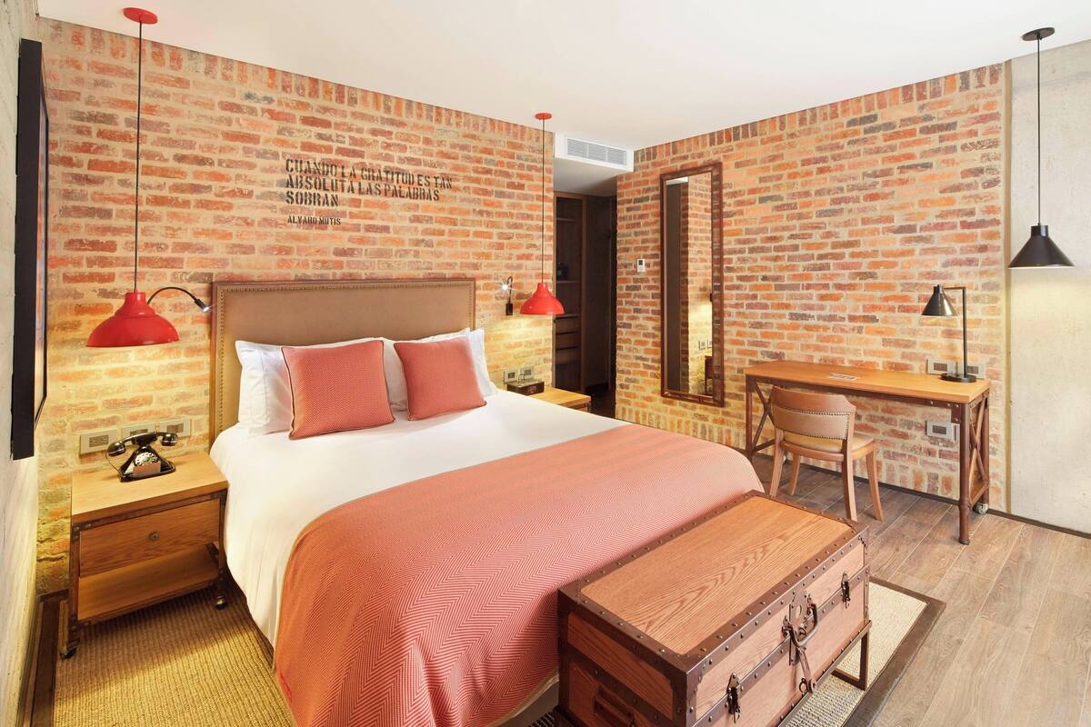 A bedroom with a brick wall, a wooden bed, a desk, and a chair.