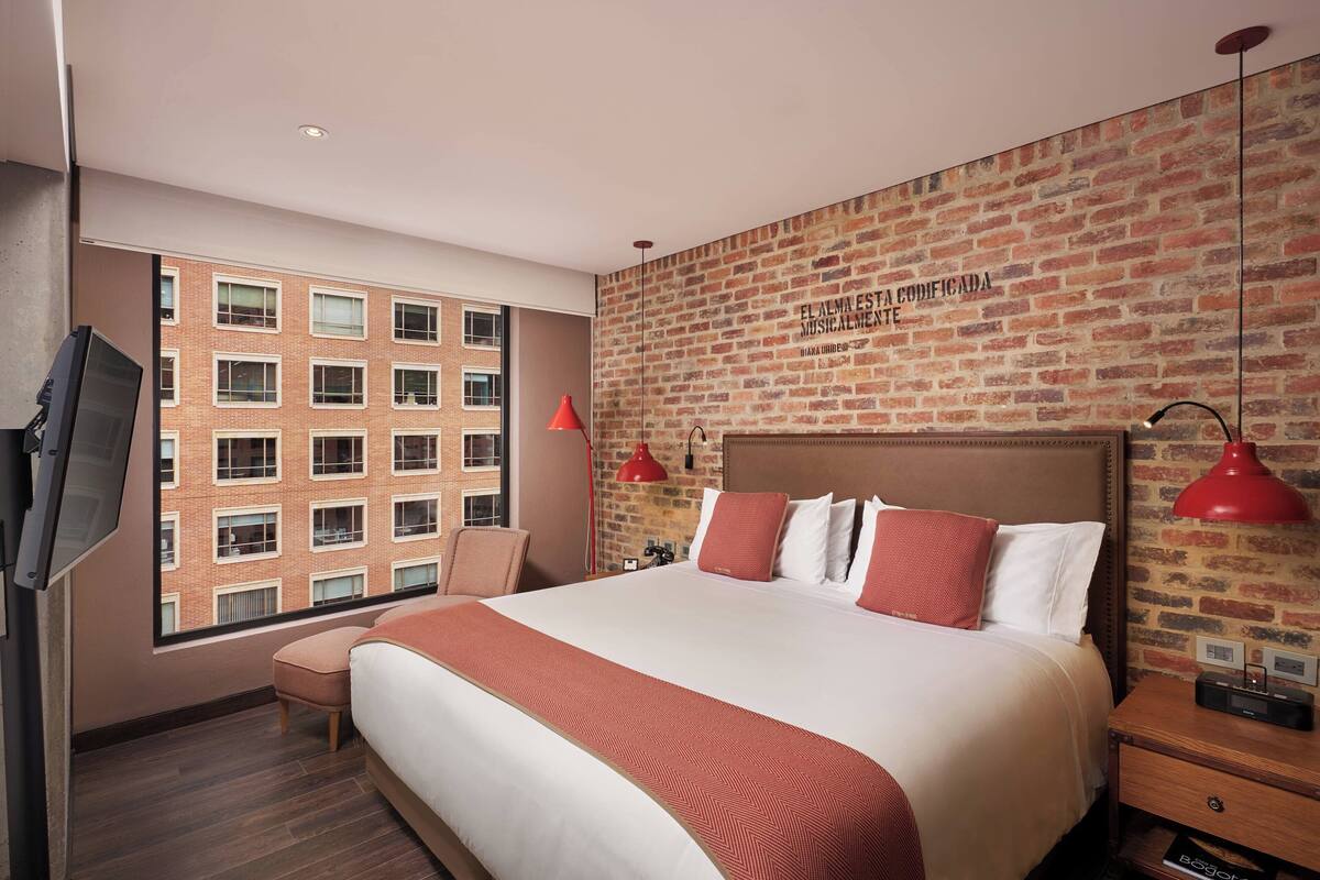 A hotel room with a large bed, a TV, a red lamp, and a brick wall with text.