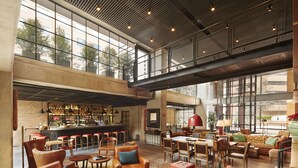 Een ruime zithoek met leren banken, houten tafels en een bar met flessen op de planken.