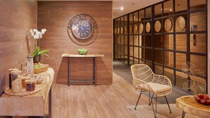 Een modern interieur met een houten wand, een ronde klok, rieten meubels en een decoratieve wand met cirkelvormige patronen.