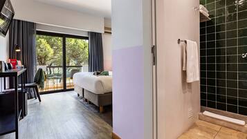 Habitación de hotel con cama, escritorio con computadora, una silla y vista a árboles a través de amplias ventanas.