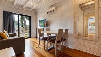 A modern room with a wooden floor, a dining table with chairs, a sofa, and a TV on a stand.