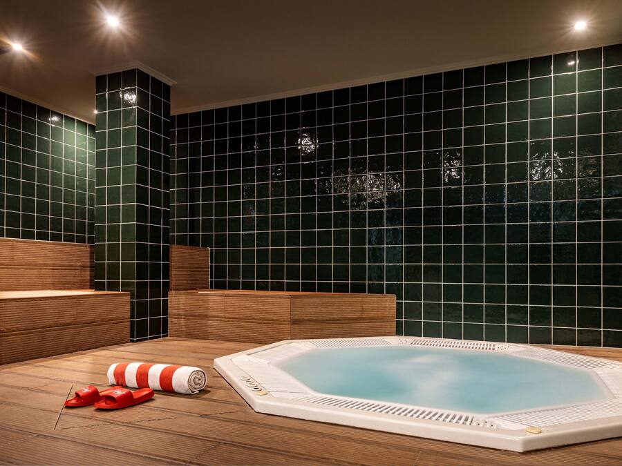 Un cuarto de spa con un jacuzzi, bancos de madera y paredes de azulejos verde oscuro.