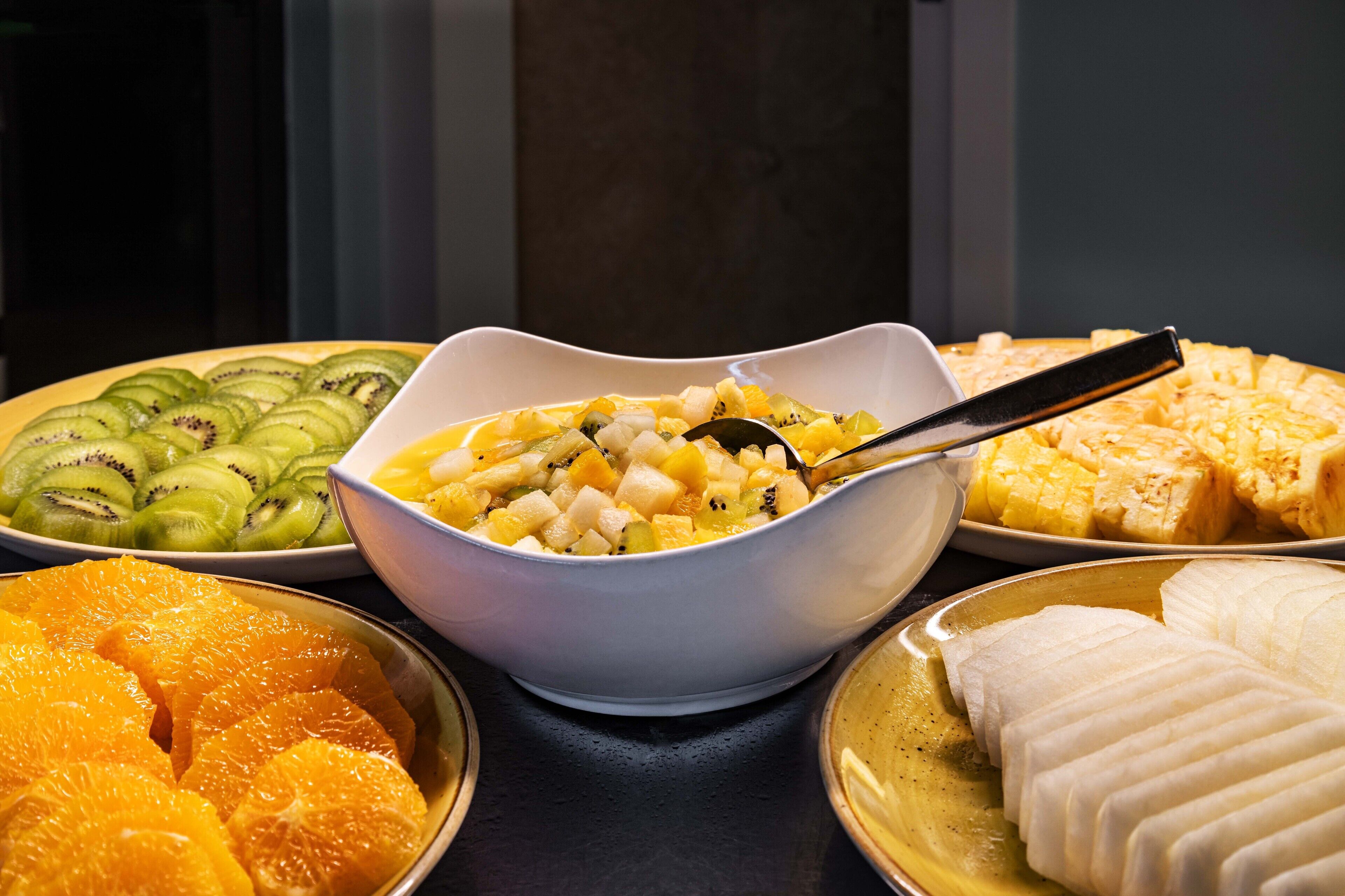 A buffet with various fruits and a bowl of mixed fruit salad.