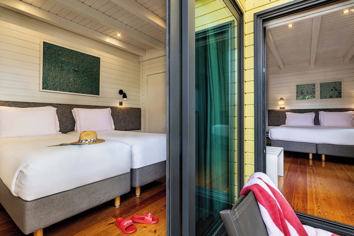 Habitación de hotel con dos camas, un ventanal con vistas y piso de madera.